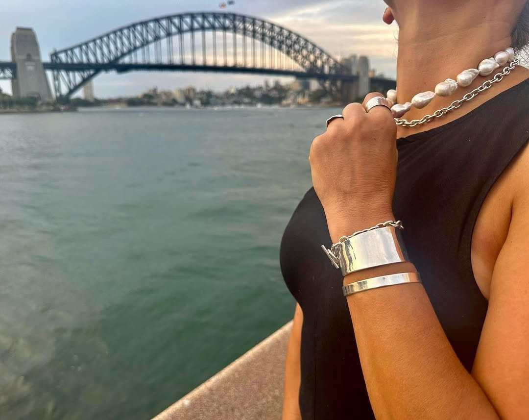 Silver pearls, chains, cuffs and rings worn beside Sydney Harbour at dusk, the Harbour Bridge across the water.