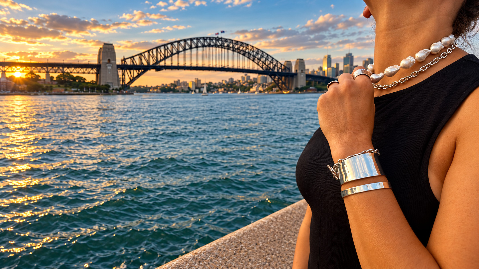 Baroque pearls, a silver chain, a wide cuff and a slim bangle worn at Sydney Harbour at sunset, the Harbour Bridge across the water.